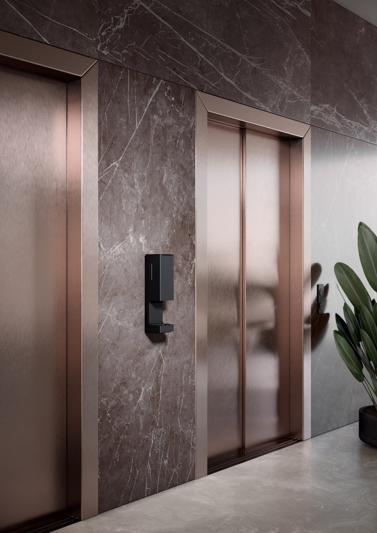 A touch-free disinfectant dispenser is installed on the wall between two lift doors